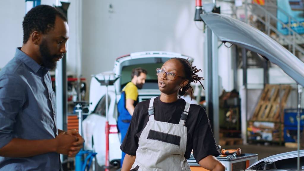 A female mechanic explains vehicle issues to the owner inside an auto repair shop.