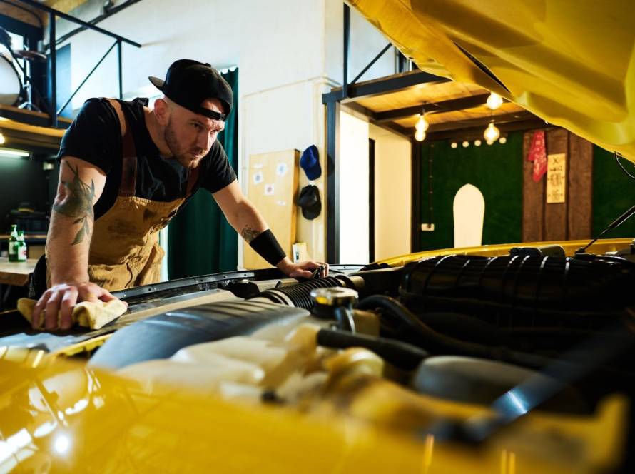 A mechanic inspects a car engine under the open hood.