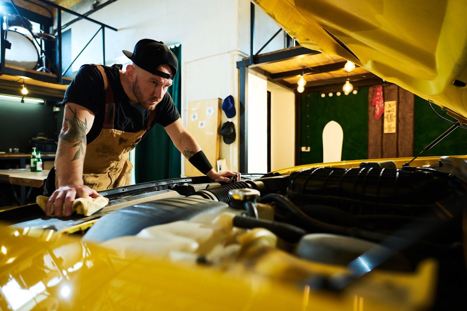 A mechanic inspects a car engine under the open hood.
