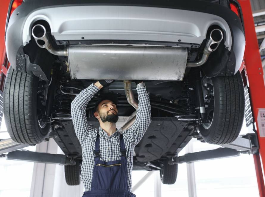 A mechanic repairs a car’s exhaust system under a lifted vehicle