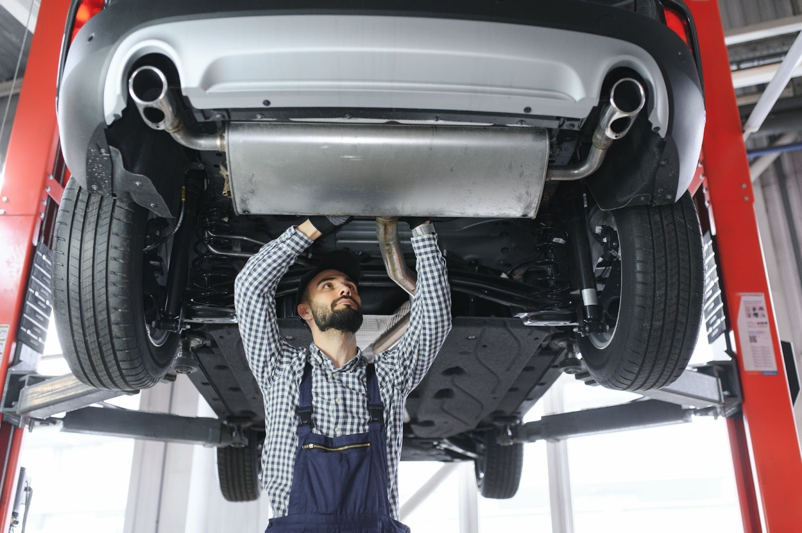 A mechanic repairs a car’s exhaust system under a lifted vehicle