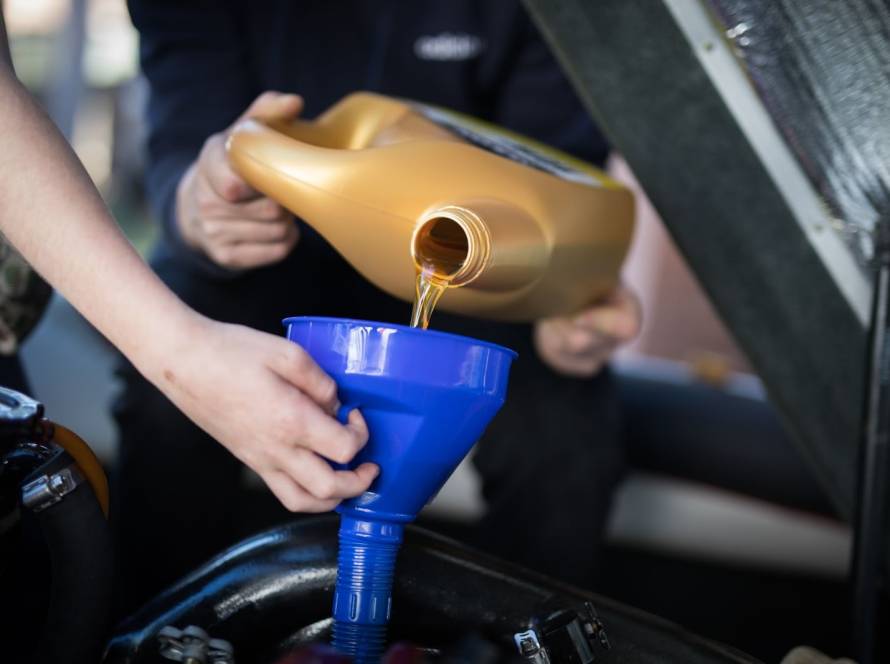A technician pours fresh motor oil into the engine while another holds a funnel. 