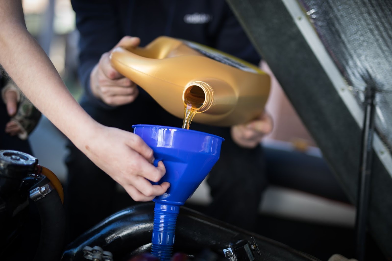 A technician pours fresh motor oil into the engine while another holds a funnel. 