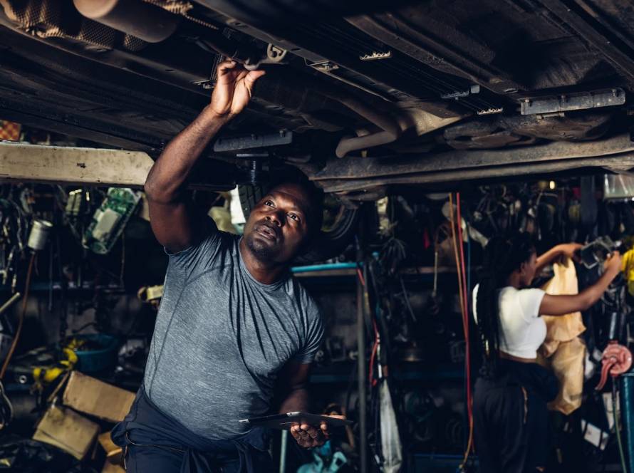A mechanic searches underneath a car while performing transmission service.