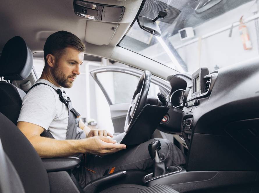 A mechanic sitting inside a vehicle using diagnostic equipment to test and monitor the car’s air conditioning system performance