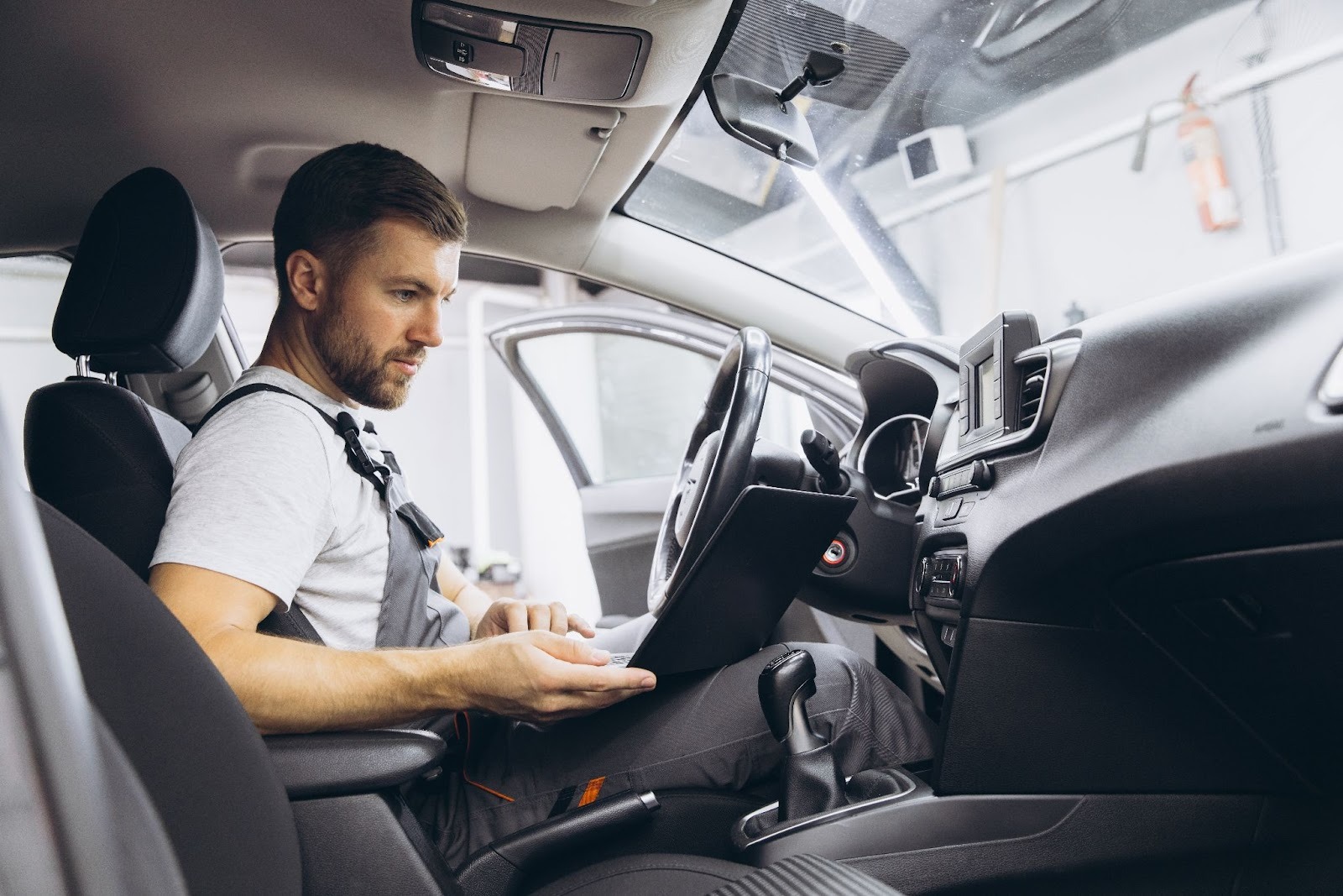 A mechanic sitting inside a vehicle using diagnostic equipment to test and monitor the car’s air conditioning system performance