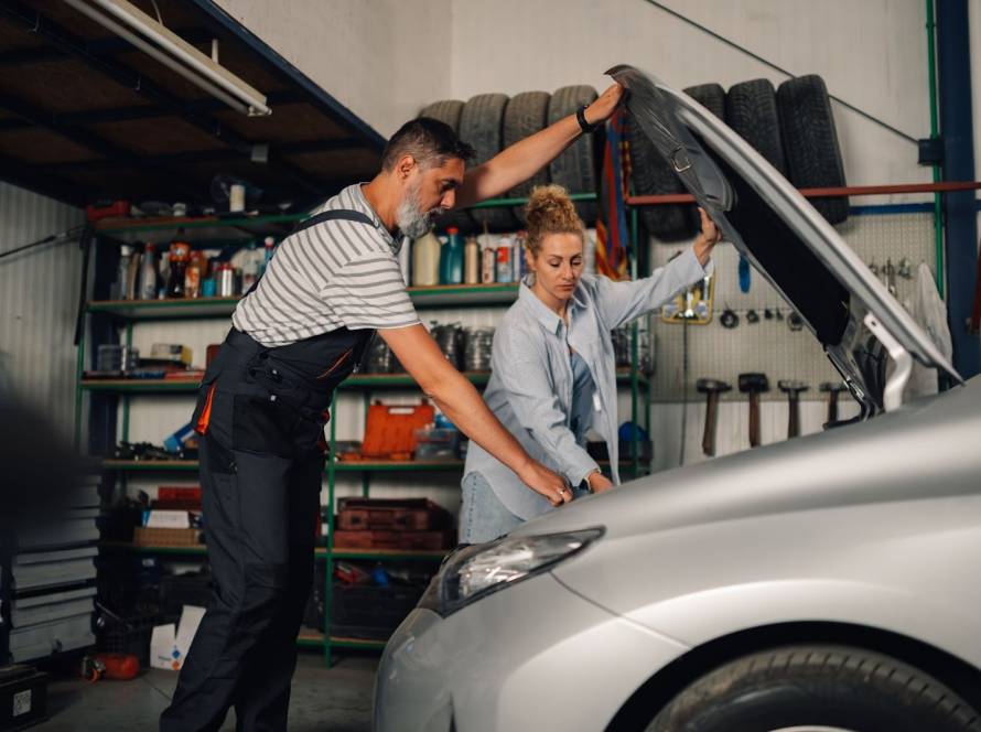 Mechanic with female customer inspecting car engine under the hood during auto service