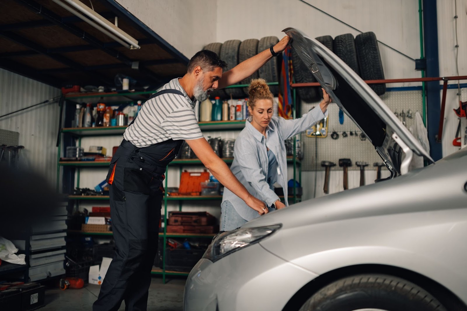 Mechanic with female customer inspecting car engine under the hood during auto service