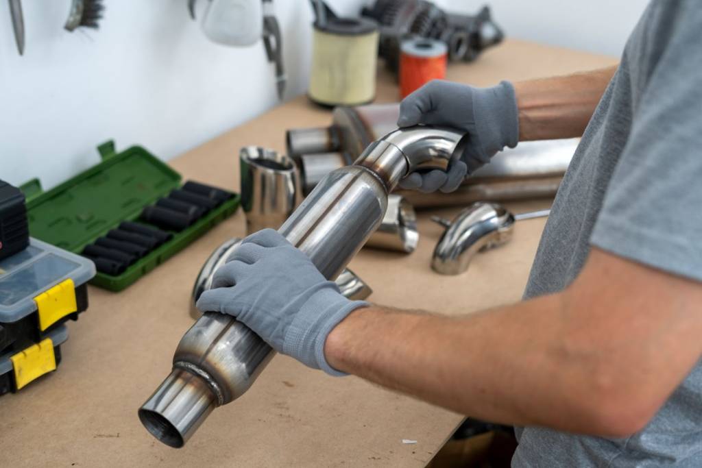 Auto mechanic examining a new muffler exhaust component to replace a damaged one.