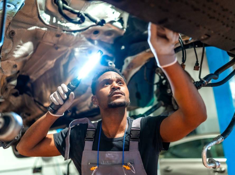 Mechanic performing a chassis inspection with a flashlight at an auto repair shop