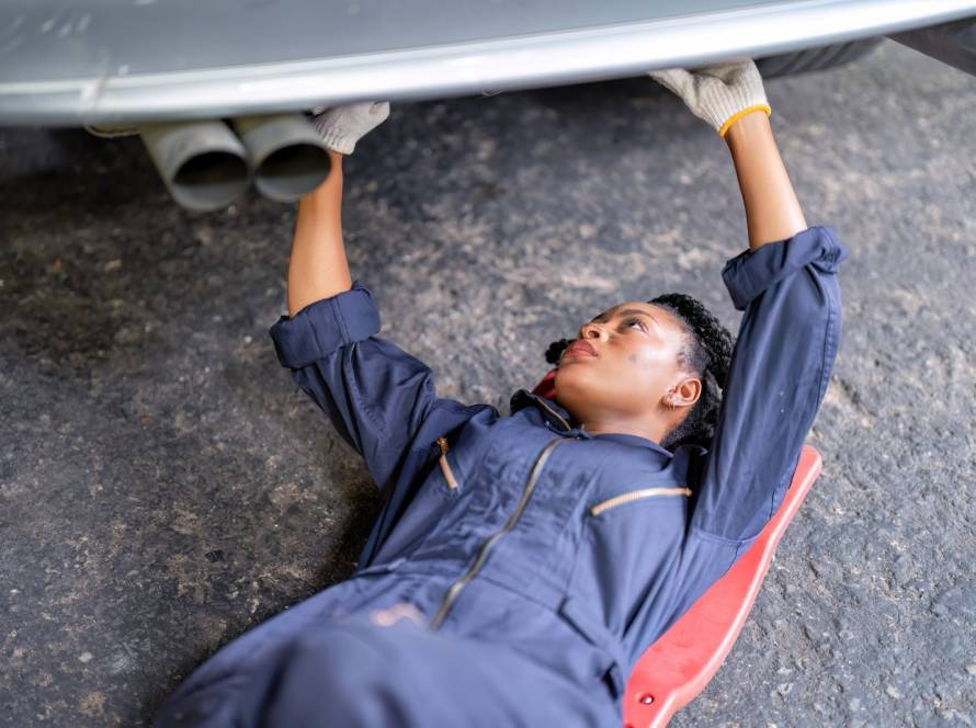 A female auto technician with a grease-stained face working under a car on exhaust repair