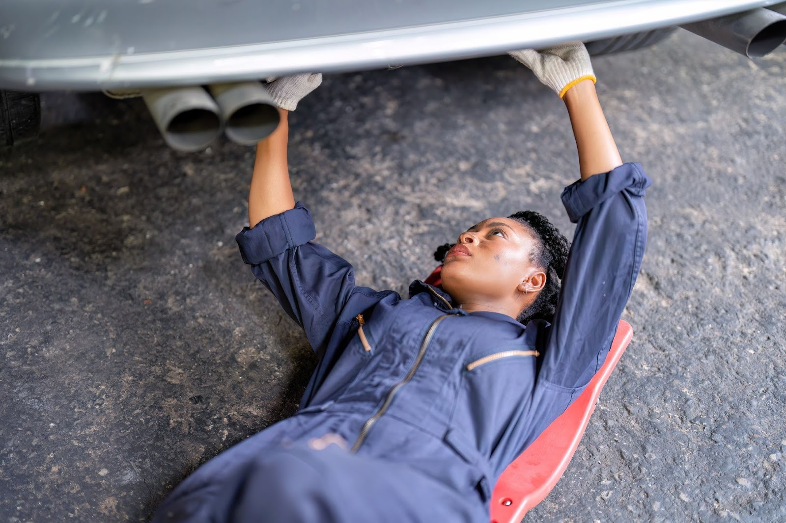A female auto technician with a grease-stained face working under a car on exhaust repair