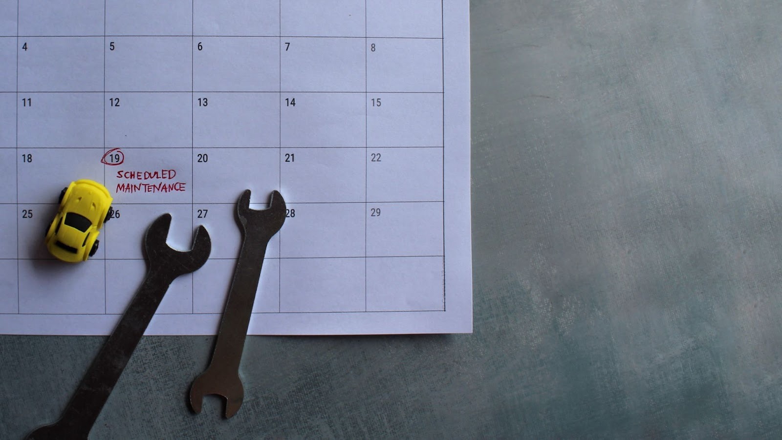 Toy vehicle and wrenches on a marked calendar highlighting scheduled maintenance dates