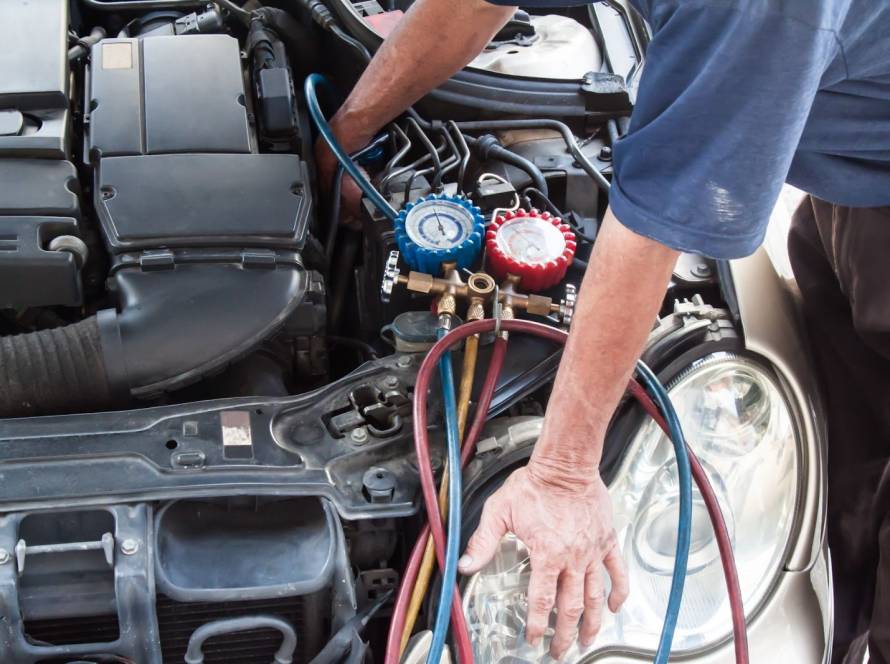 Auto mechanic measuring refrigerant pressure on a vehicle’s cooling system with a manometer