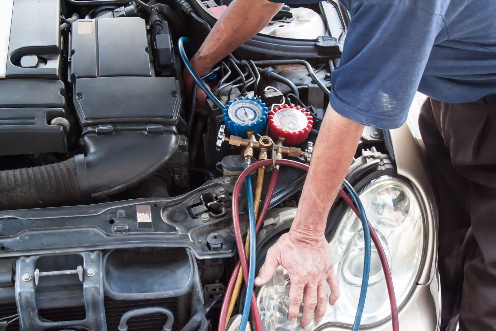 Auto mechanic measuring refrigerant pressure on a vehicle’s cooling system with a manometer